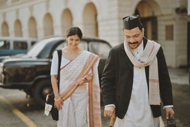 一对身着复古风格的印度夫妇在孟买的殖民建筑中漫步，背景是一辆老式汽车。图片下载