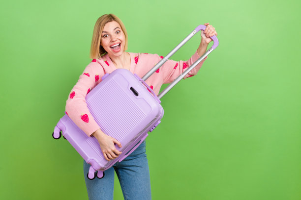 漂亮年轻女孩的照片肖像，兴奋地穿着时尚的粉色草莓印花服装，手提紫色行李箱，背景为绿色。图片下载