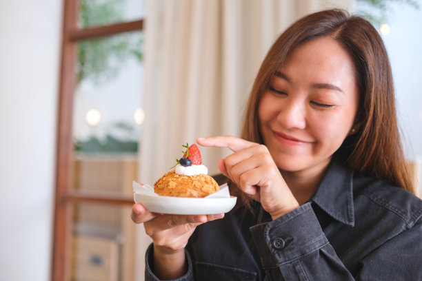一位女性在咖啡馆里手持并指向草莓泡芙的肖像照片图片下载