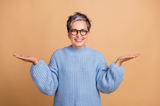 可爱的祖母的照片肖像，双手托着空白空间，穿着时尚的蓝色针织服装，背景为米色。图片下载