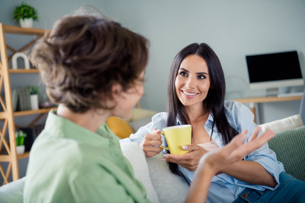 可爱的年轻女士们穿着衬衫，坐在沙发上聊天，喝茶，室内房间的照片图片下载