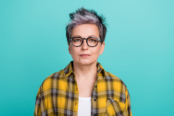 吸引人的退休女性的照片肖像，穿着时尚的黄色格子衣服，面向镜头，背景为水绿色。图片下载