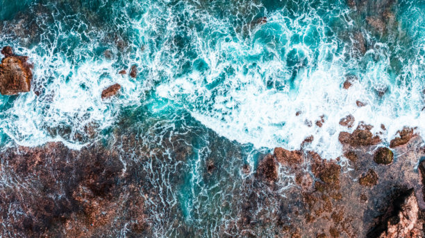 阳光明媚的夏季海岸线，海浪拍打着海边悬崖的航拍照片。图片下载