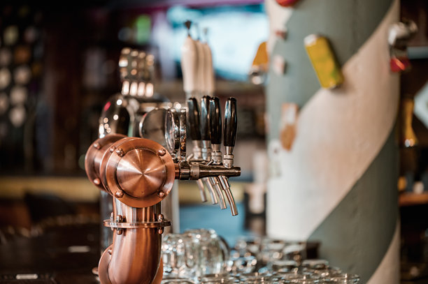 酒吧内一个抛光铜和不锈钢啤酒龙头系统的特写，配有多个把手用于倒生啤酒。背景中可见准备使用的酒杯。图片下载