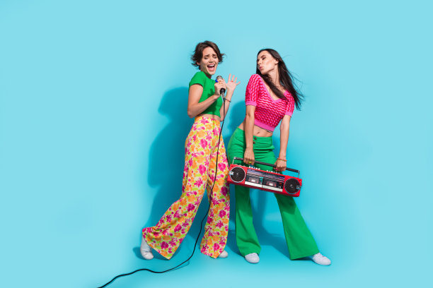 两个快乐的好朋友在蓝色背景下，尽情享受音乐会，手持音响，尽情歌唱的全身照片图片下载