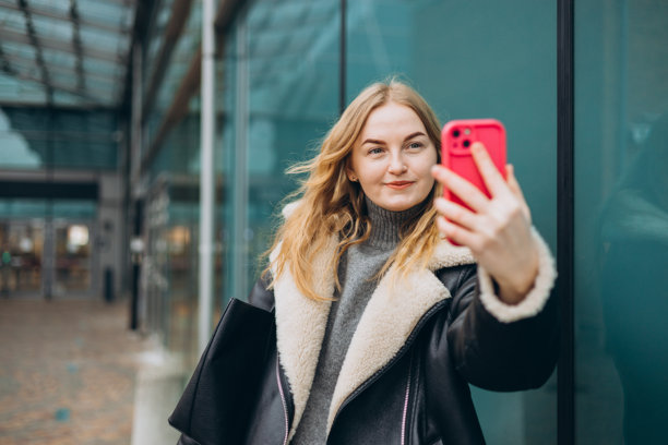快乐的金发女性在现代城市背景下自拍。迷人的女性穿着时尚的服装，享受美好时光。高质量照片。图片下载