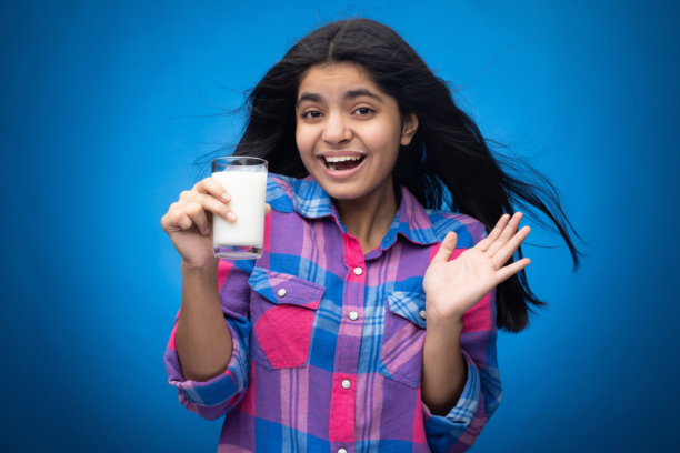 年轻女孩在蓝色背景下喝牛奶的肖像照片图片下载