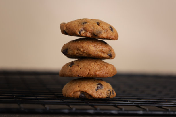 黑色冷却架上叠放的巧克力曲奇饼干，背景为深色木桌和米色墙壁。特写照片。图片下载