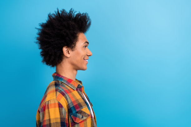 侧面照片，满意的男士留着卷发，穿着格子衬衫，注视着蓝色背景上空荡荡的销售空间。图片下载