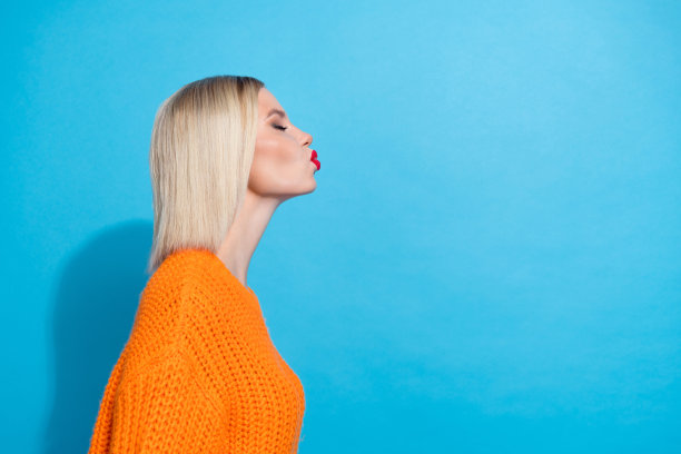 侧面照片，迷人的女性，短发，穿着针织毛衣，亲吻空白空间，背景为蓝色。图片下载