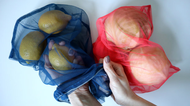 生态网袋中的水果和蔬菜照片。白色背景。女性手正在拿出柠檬。图片下载