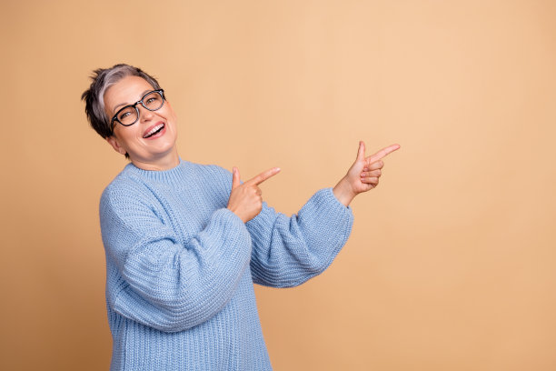 可爱的祖母照片肖像，手指指向空白处，穿着时尚的蓝色针织服装，背景为米色。图片下载