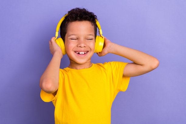 可爱的年轻男孩在紫色背景下穿着黄色衣服，戴着耳机，享受乐趣的照片肖像图片下载
