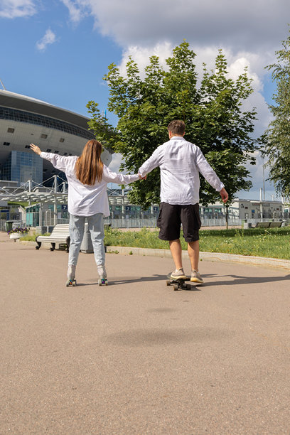 年轻情侣在公园里滑旱冰和滑板。快乐的女孩和男孩在温暖的夏日一起运动。竖版照片图片下载