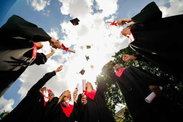 低角度拍摄的照片，展示了一群同学在户外抛掷学位帽庆祝毕业。图片下载