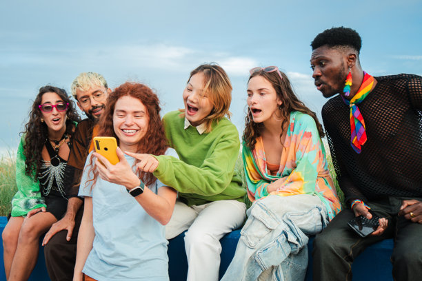 一群年轻人，代表不同种族，在会议期间愉快地使用智能手机。成年朋友们在社交媒体应用上分享照片和交流信息。图片下载