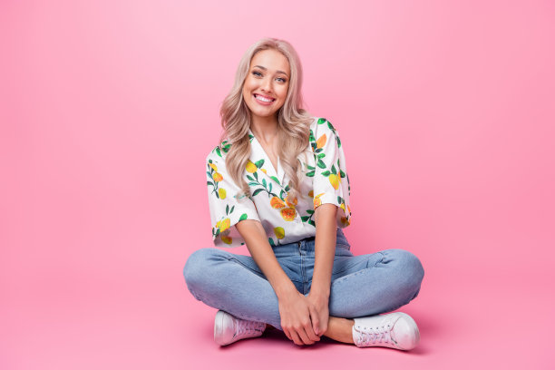 全身照片，纤细年轻女孩模特以交叉腿的姿势坐在花园中，等待她的朋友，背景为粉色。图片下载