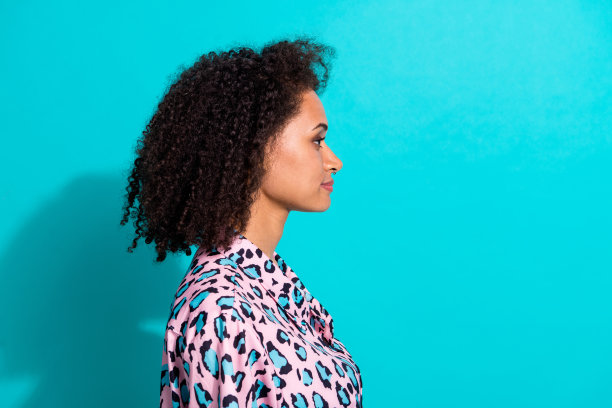 可爱的女孩侧面照片，穿着时尚衣服，正在进行烫发美容程序，背景为青色。图片下载