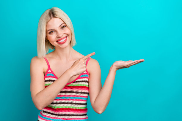 可爱的年轻女士的照片肖像，手掌指向空白处，穿着时尚的条纹服装，背景为水绿色。图片下载