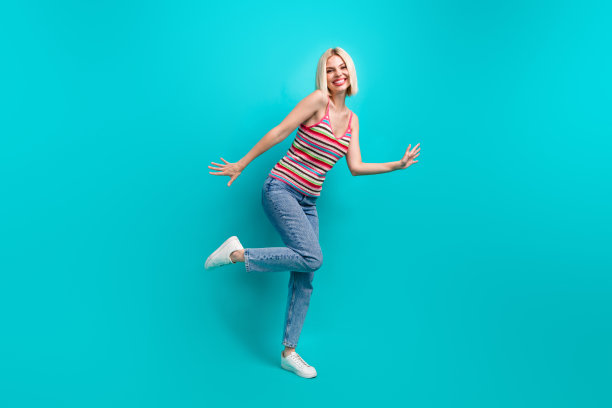 穿着条纹背心的快乐女孩在青色背景下跳舞，尽情享受乐趣的全身照片图片下载