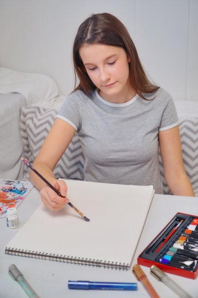 小女孩在桌子上用丙烯画画并思考的竖拍照片图片下载