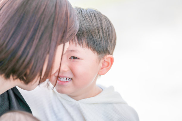 在福冈的公园里，春天，一位三十多岁的妈妈与她三岁的儿子共享温馨时刻。他们在自然环境中相视而笑。这张照片捕捉了一个温暖而真实的家庭时刻。图片下载