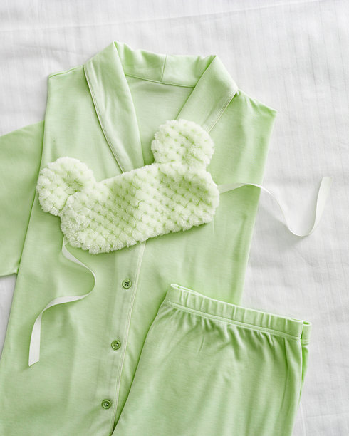 俯视折叠的淡绿色女性睡衣和毛绒睡眠眼罩，放在白色床上。简约的平铺舒适睡衣，适合睡觉和放松。时尚睡衣的美学生活方式照片。图片下载