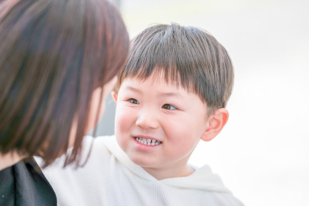 在福冈的公园里，春天，一位三十多岁的妈妈与她三岁的儿子分享着温馨的时刻。他们在自然环境中相视而笑。这张照片捕捉了一个温暖而真实的家庭时刻。图片下载