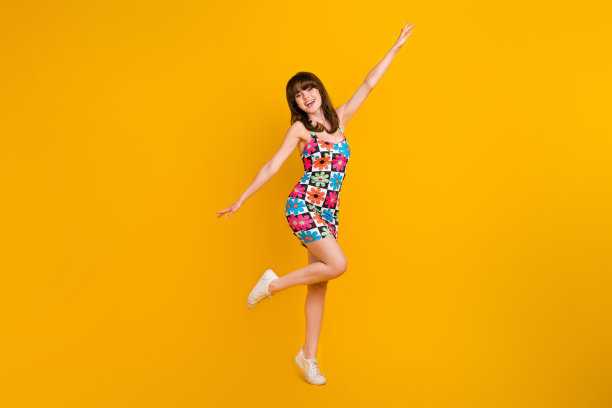 穿着花卉印花服装的无忧无虑的时尚女性在黄色背景下尽情舞蹈，享受乐趣的全身照片图片下载