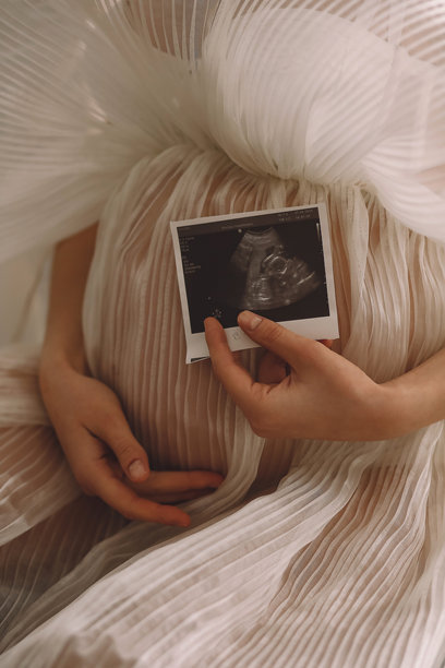 穿着美丽象牙色裙子的孕妇手持超声波照片，靠近孕肚。母亲身份的概念图片下载