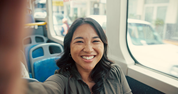 女性在公交车上自拍，面带笑容，记录旅程回忆，适合社交媒体发布或观光冒险。肖像，公路旅行或公共交通摄影，适合通勤和更新个人资料照片。图片下载