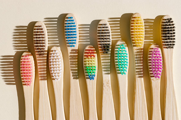 环保竹牙刷，彩色刷毛在阳光下，深色阴影映衬在米色背景上。可持续生活理念，极简风格美学照片，俯视视角的木质牙刷组合。图片下载