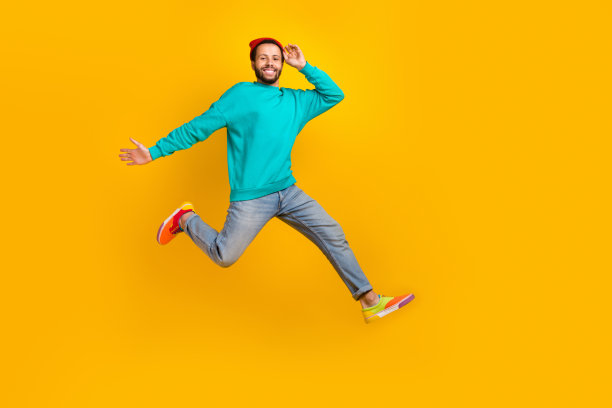 全身照片，心情愉快的古怪男士穿着牛仔裤，手持红色毛线帽，飞奔购物，背景为黄色。图片下载