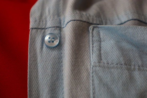 蓝色布料的特写，带有纽扣和缝线，背景为鲜艳的红色。这张图片非常适合展示服装细节、纺织品或与时尚相关的项目。图片下载