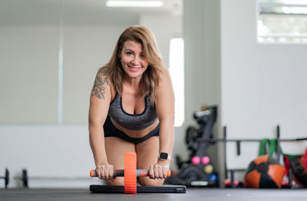 微笑的女性在健身房使用腹部轮锻炼 - 股票照片。图片下载