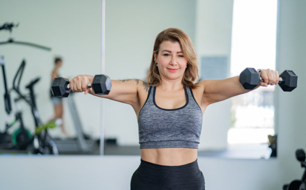 女性在现代健身房用哑铃训练肩部 - 股票照片。图片下载