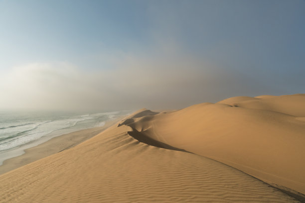 纳米比亚三明治港的壮丽景色。高耸的金色沙丘倾泻而下，直达大西洋的海岸。这张照片传达了一种宁静感和自然的宏伟。图片下载