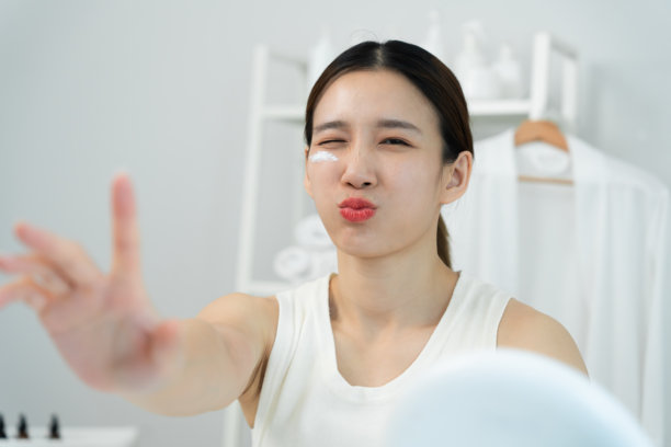 美丽的亚洲女性微笑着使用护肤霜。健康女性的面孔涂抹护肤霜和化妆品。护肤霜广告，抗皱，婴儿般的肌肤，美白，保湿，收缩毛孔精华。图片下载