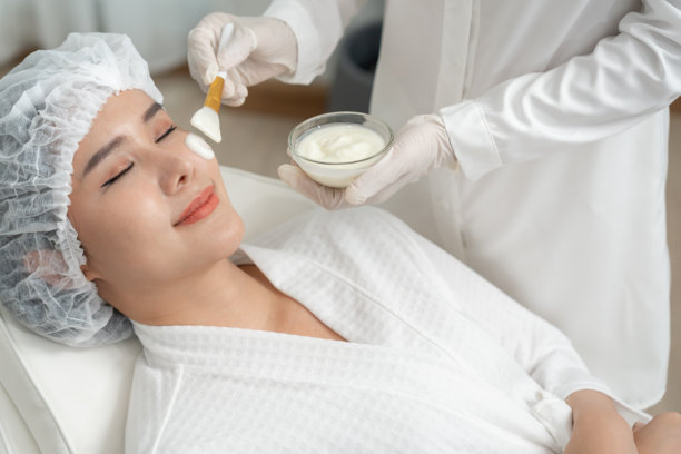 美丽的女性正在接受面部水疗和护理。健康女性的面部涂抹面霜。皮肤霜的广告，抗皱、婴儿般的肌肤、美白、保湿、收缩毛孔精华。图片下载