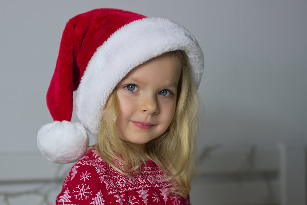 小金发女孩戴着红色圣诞帽，穿着睡衣，背景有圣诞装饰，微笑着看向镜头，孩子的新年服装肖像，冬季假日图片图片下载