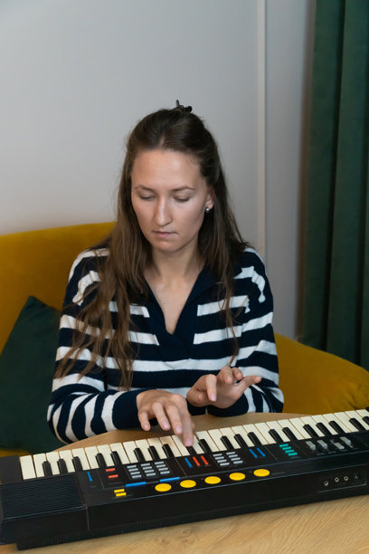 年轻女性舒适地坐在鲜艳的黄色沙发上，正在一张木桌上演奏复古合成器，沉浸在创意和声音中，周围是她时尚的现代公寓。竖版照片图片下载