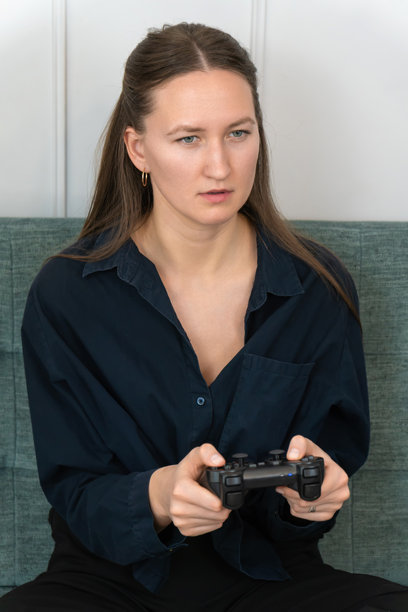 年轻女性坐在舒适的沙发上，手握游戏手柄，专注地玩着视频游戏，脸上带着严肃的表情。竖版照片图片下载