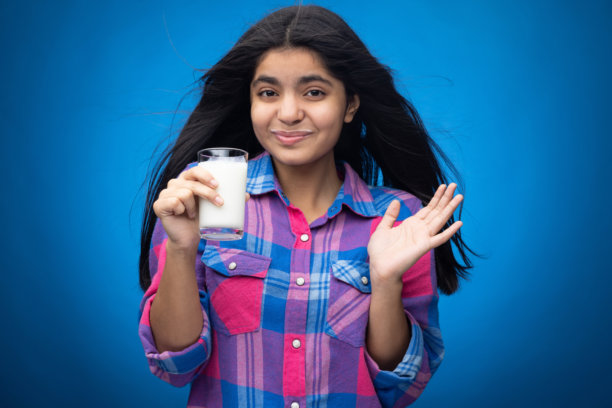 年轻女孩在蓝色背景下喝牛奶的肖像照片图片下载