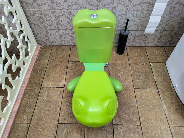 浴室里有一个绿色的儿童青蛙形状的马桶，背景是米色瓷砖。图片下载