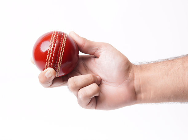 特写照片：男性保龄球手强有力地握住一颗闪亮的红色测试板球，背景为白色。图片下载