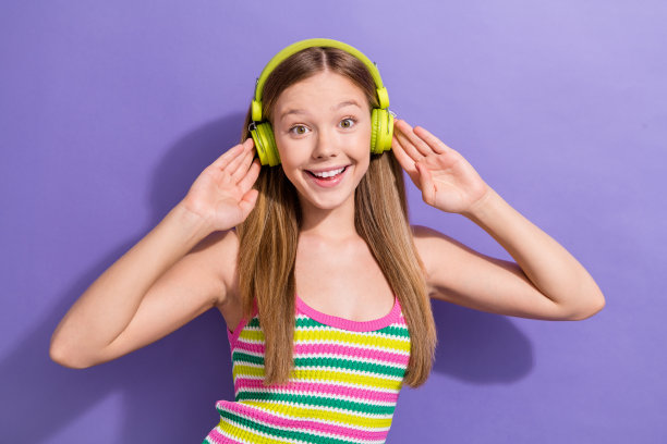 漂亮的金发少女在紫色背景下，佩戴耳机，穿着时尚的条纹服装，拍摄的照片肖像。图片下载