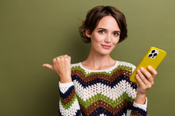 可爱的年轻女士的照片肖像，穿着时尚的印花针织衣服，指向空白空间，背景为卡其色。图片下载