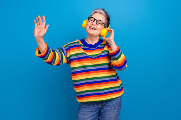 积极平和的老年女士闭着眼睛，手臂触碰耳机，独自在蓝色背景下跳舞的照片图片下载