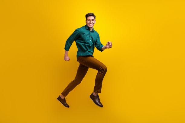 穿着时尚衣服的快乐男士在黄色背景下奔跑，展现全身照片。图片下载