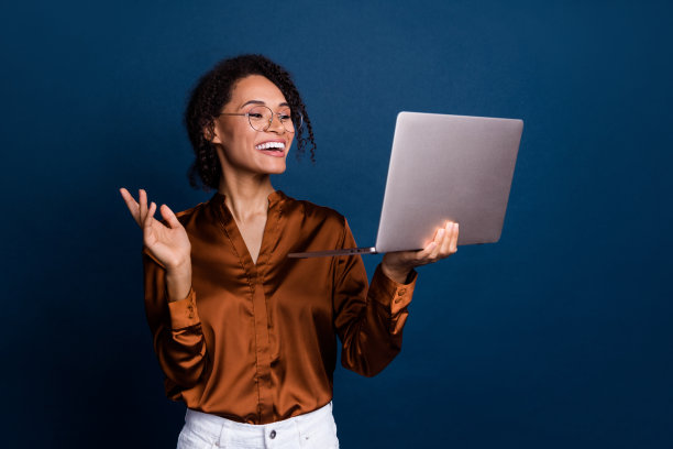 漂亮年轻女孩在深蓝色背景下穿着时尚的棕色丝绸正装，正在进行HR面试，手持笔记本电脑的照片肖像。图片下载